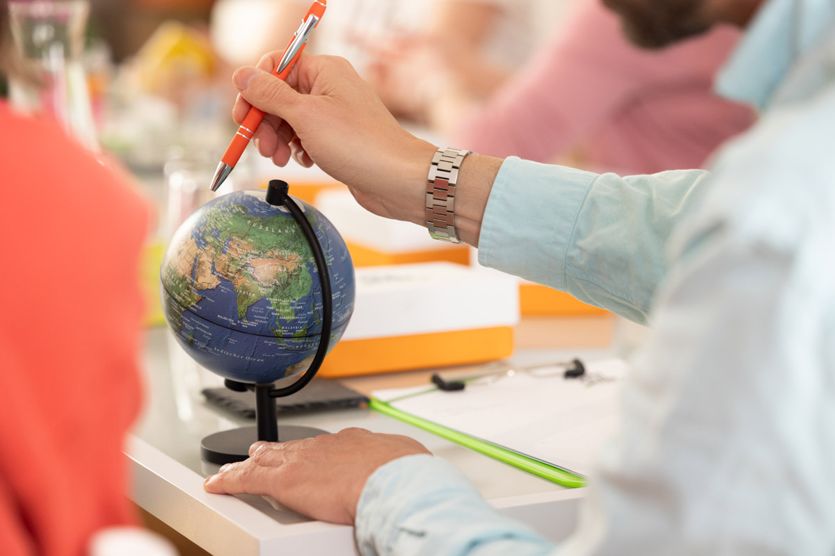 A small globe on a table, with a workshop participant pointing to particular place on it using a pen.